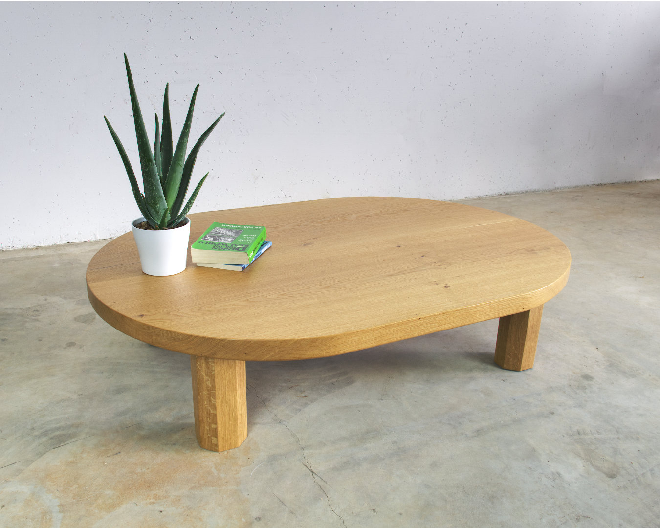 seitenansicht couchtisch massivholz eiche oval mit achteckigen beinen darauf pflanze und buch